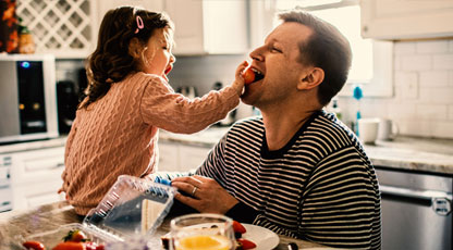 A little girl feeding her dad in the kitchen while cooking together