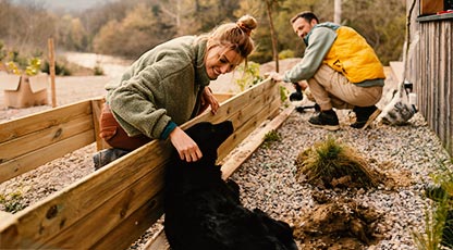 Image of two people building a garden wall. One is petting a dog.