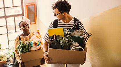 Two people walking up the stairs carrying overflowing boxes