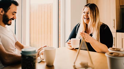Image of two people laughing in an office setting drinking coffee