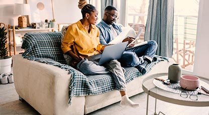 Couple sittin gon ouch looking at computer and paperwork