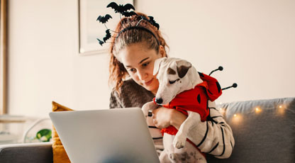 Image of a women holding a dog while using a laptop while wearing Halloween costumes
