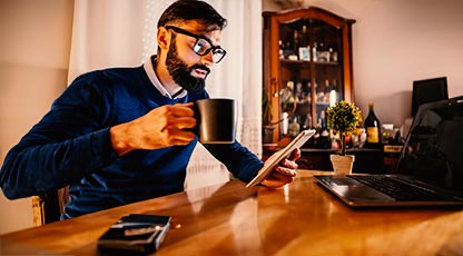 Image of person at a table with a coffee mug looking at their phone