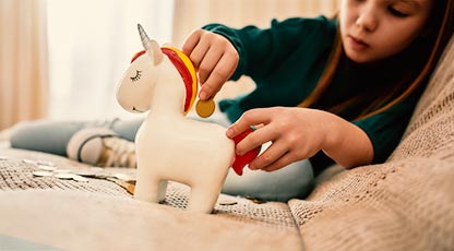 Image of young child putting coin into unicorn piggy bank