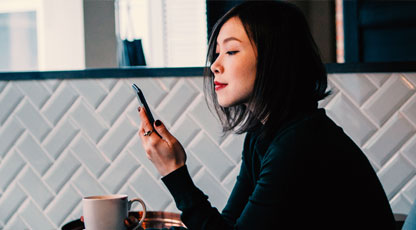 Image of person sitting with a cup of coffee looking at phone