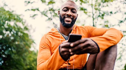 An adult smiles while listening to something on a smartphone through wired earbuds