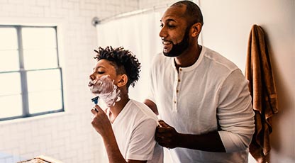 A parent teaches their child how to shave in a bright bathroom