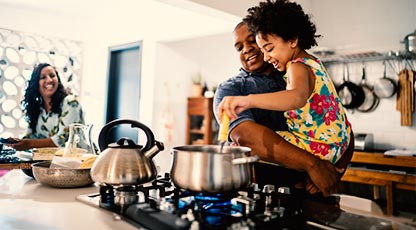 A parent holds a child while the child stirs something on the stove