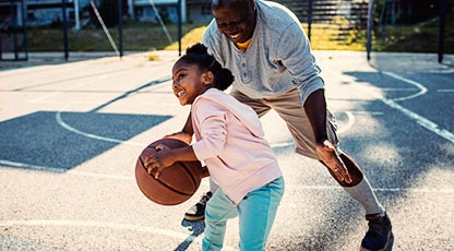 A parent and young child playing basketball outside