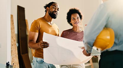 A couple reviews blueprints while speaking with a construction worker