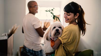 A person smiles while holding a dog as their partner looks on and smiles