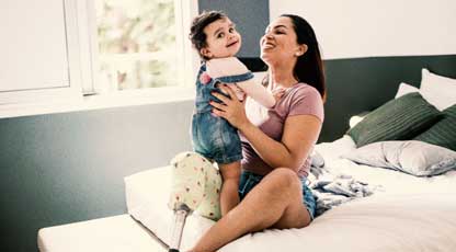 A happy parent plays with their toddler child on a bed