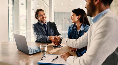 Image of people smiling and shaking hands at a a table with a computer. 