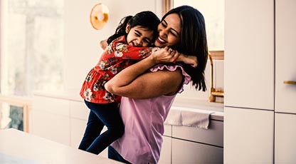 A smiling parent holds up their young child who is laughing