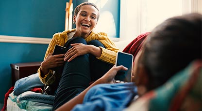 A young adult laughs with the person across from her as both people hold onto their phones