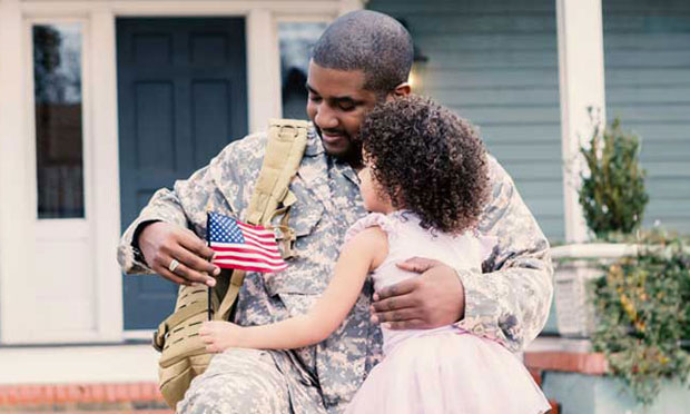 Image of a male soldier holding a flag and a hugging a young child in front of a house