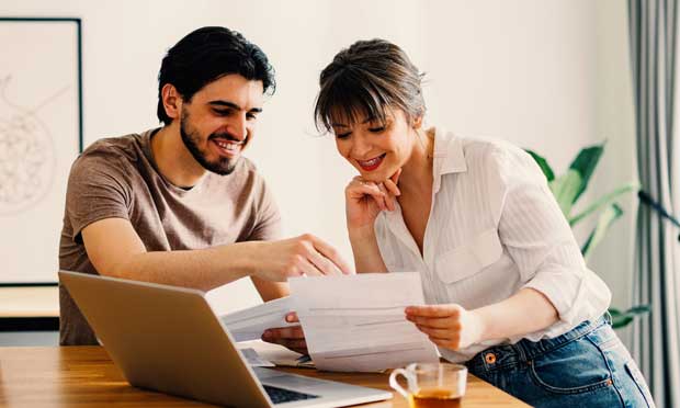 image of two young people at a dining table looking at a computer and a monthly bill