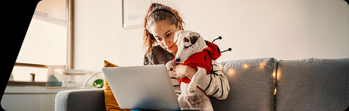 Image of a women holding a dog while using a laptop while wearing Halloween costumes