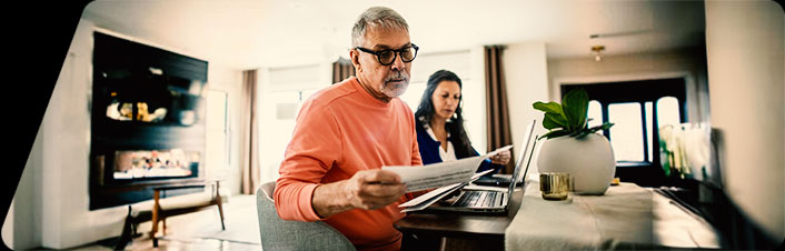 Image of two people at a table with laptops and looking at documents