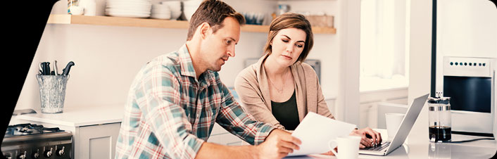 Image of two people sitting in a kitchen with a computer looking at a document