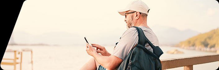 Image of a man looking at phone and standing outside overlooking the water