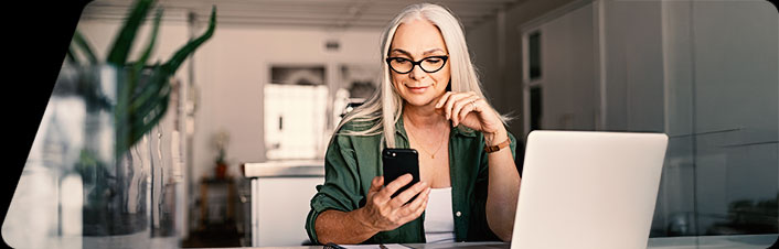 Image of person sitting at  desk with computer, looking at phone