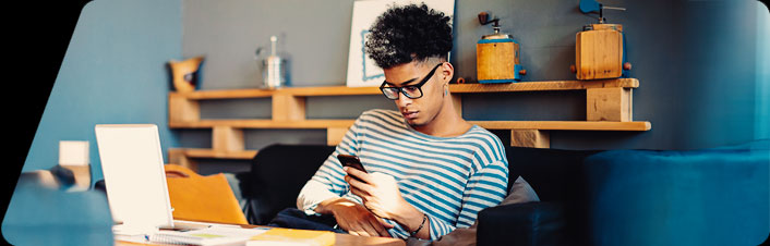Image of a young person using phone and laptop at a table
